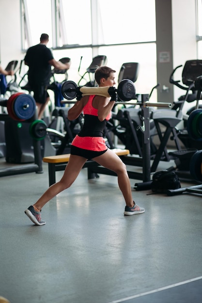 Vista posteriore di una donna sportiva con i capelli corti che indossa in rosa che lavora in palestra da sola e distoglie lo sguardo Donna in forma che fa esercizio con il concetto di Sportlife con bilanciere