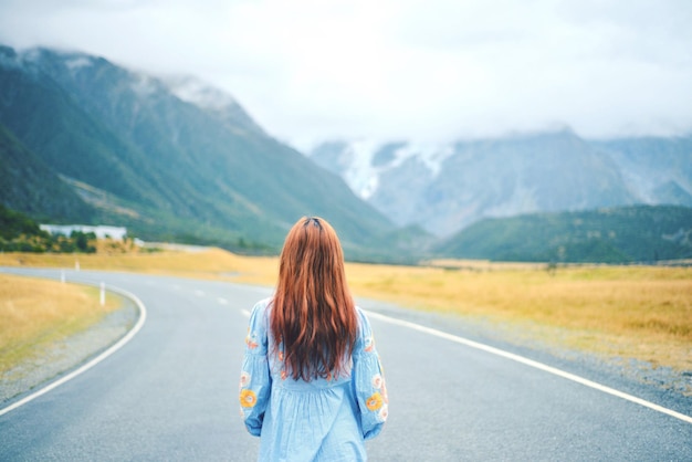 Vista posteriore di una donna sulla strada contro la catena montuosa