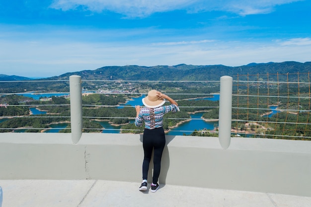 Vista posteriore di una donna turistica con cappello che contempla la natura in Guatape Colombia da Penol stone