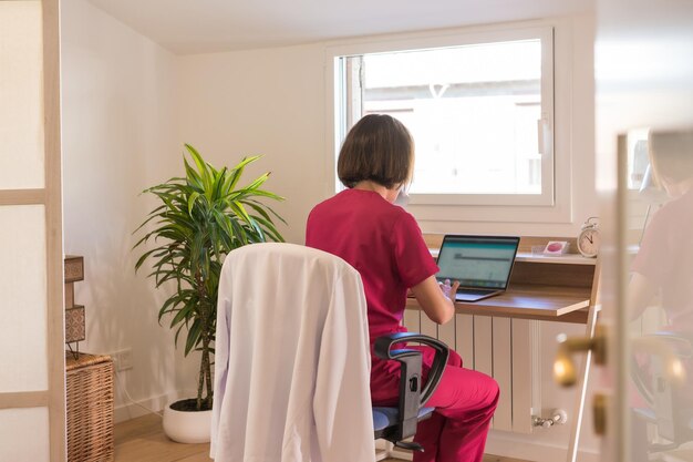 Vista posteriore di una dottoressa che utilizza un laptop mentre lavora da un ufficio a casa