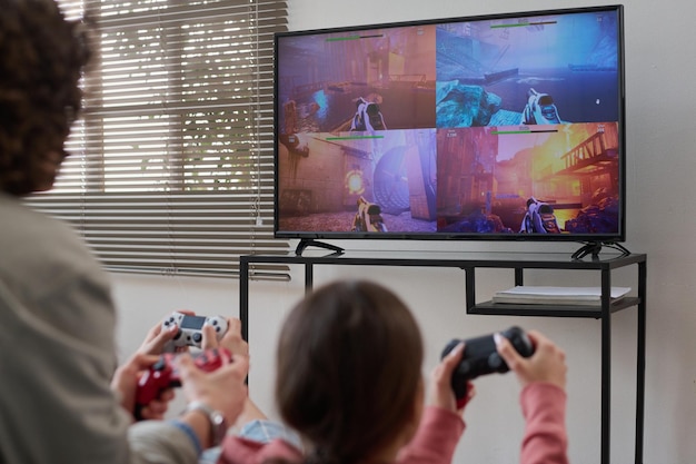 Vista posteriore di una famiglia di due persone che giocano insieme ai videogiochi seduti davanti allo schermo della tv nella stanza