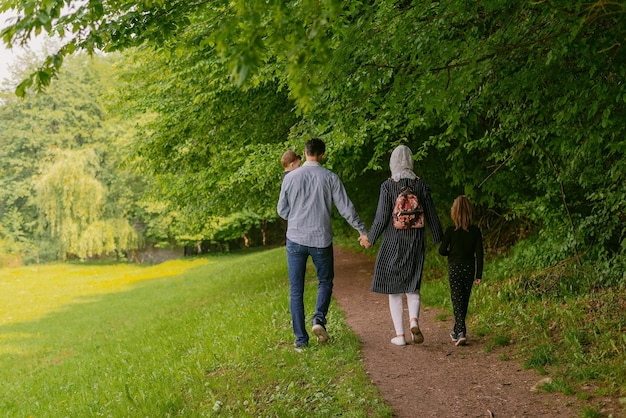 Vista posteriore di una felice famiglia musulmana che cammina insieme mentre si tiene per mano nel parco estivo