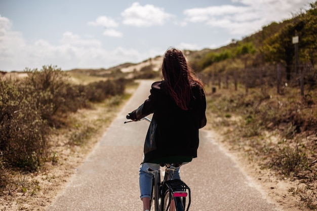 Vista posteriore di una giovane bella ragazza cammina single sulla bicicletta sulla strada in tempo di giorno pieno di sole.