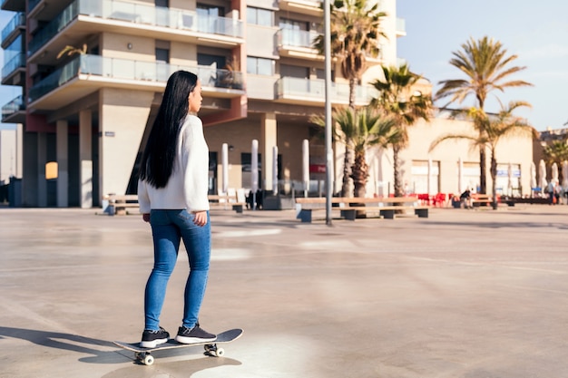 Vista posteriore di una giovane donna asiatica in sella a uno skateboard in città