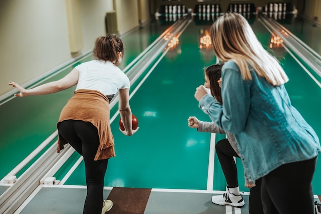 Vista posteriore di una giovane donna che lancia la palla da bowling mentre i suoi amici fanno il tifo.