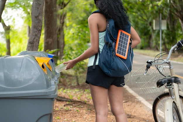 Vista posteriore di una giovane donna che raccoglie rifiuti nel parco Ha uno zaino con un pannello solare per caricare lo smartphone