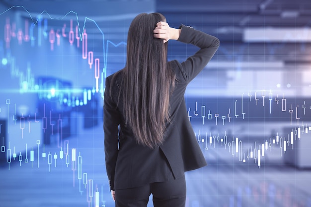 Vista posteriore di una giovane donna d'affari stressata in tuta in piedi in un ufficio moderno interno con grafico forex Crisi e concetto commerciale Doppia esposizione