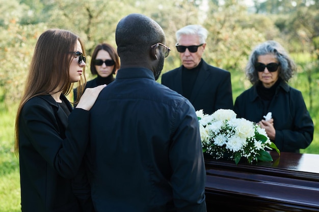 Vista posteriore di una giovane donna in abiti da lutto che sostiene il marito al funerale