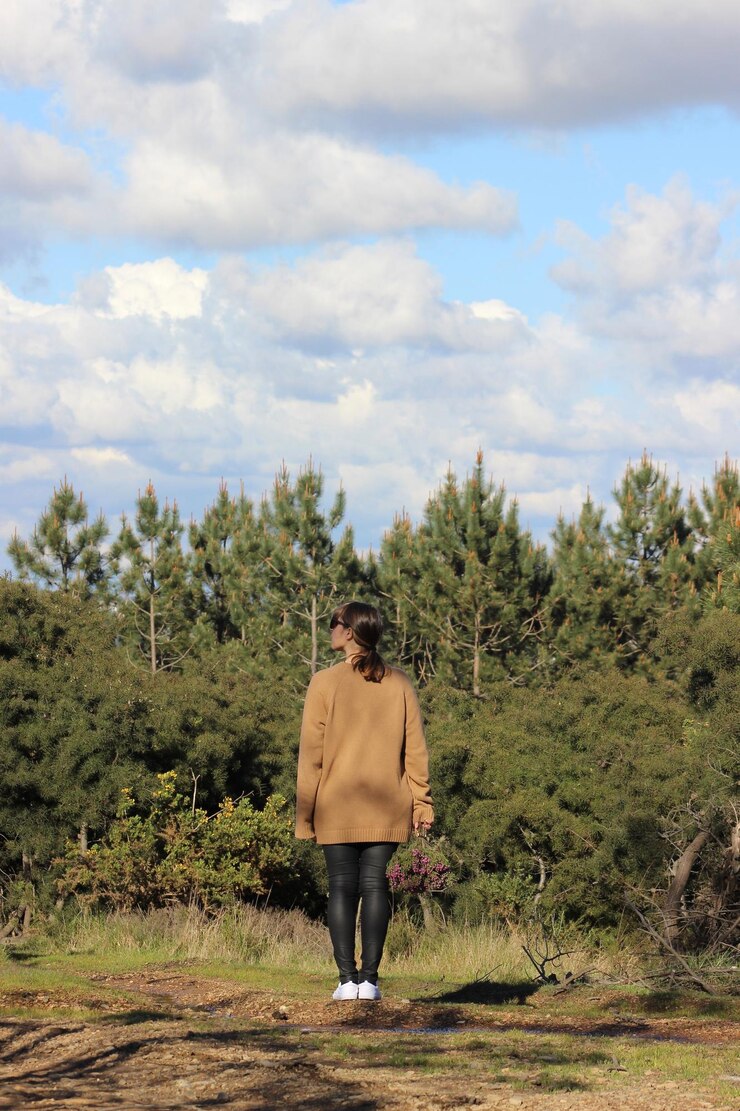Foto vista posteriore di una giovane donna in piedi sul campo contro gli alberi