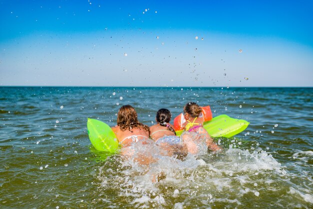 Vista posteriore di una giovane mamma di famiglia positiva e di due figlie nuotano su un materasso ad aria gialla in mare