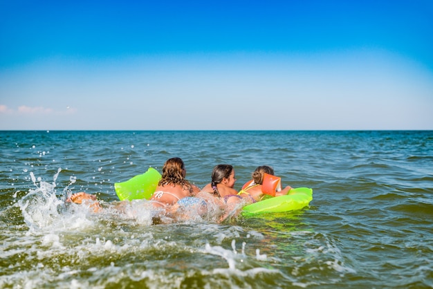 Vista posteriore di una giovane mamma di famiglia positiva e due piccole figlie nuotano su un materasso ad aria giallo in mare in una soleggiata giornata estiva durante le vacanze. Concetto di relax. Copyspace