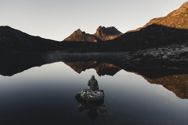 Vista posteriore di una persona sulla roccia in mezzo a un lago calmo contro la montagna