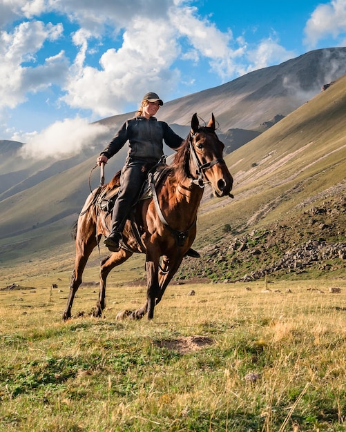 Vista posteriore di una ragazza caucasica a cavallo che galoppa attraverso una valle di montagna contro il cielo