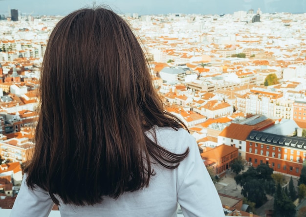 Vista posteriore di una ragazza che guarda lo skyline della città di Madrid dal tetto di un edificio.