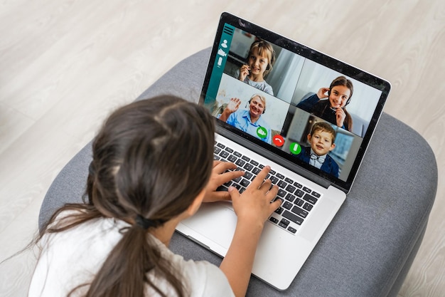 Vista posteriore di una ragazza seduta a casa, parlare con una lezione di videochiamata online con insegnante o tutor, studentessa adolescente impegnata in una conversazione in webcam, studiare l'app per conferenze web a distanza sul laptop