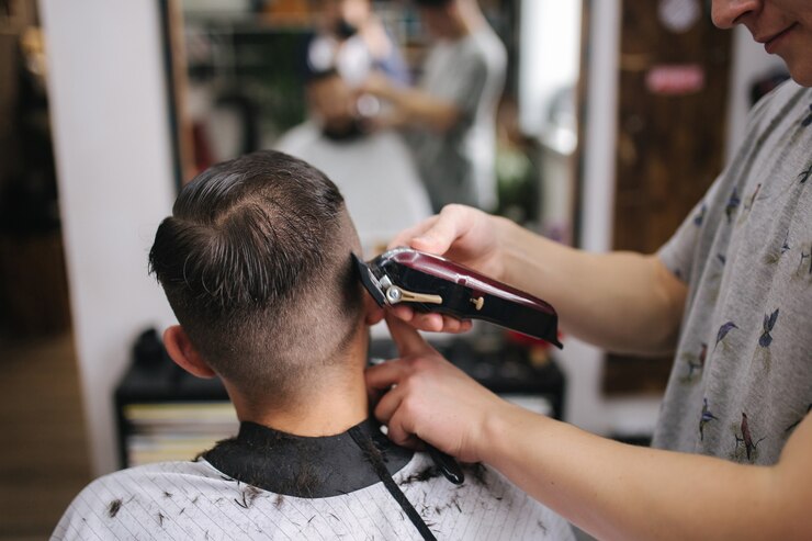 Vista posteriore di uomini nel salone di bellezza. Taglio di capelli maschile in un negozio di barbiere. Nuovo stile di taglio di capelli 2021. Il parrucchiere professionista usa un tagliacapelli per frangiare i capelli
