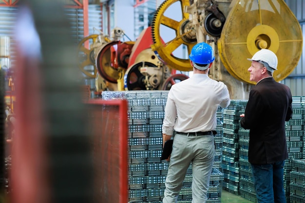 Vista posteriore dietro e vista posteriore tornio e macchina per stampaggio metallo Uomo d'affari caucasico e ingegnere di fabbrica con casco rigido che parla e discussione presso la fabbrica di produzione dell'industria pesante