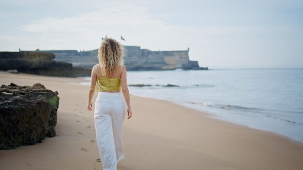 Vista posteriore donna che cammina sulla spiaggia di sabbia che si gode la sera paesaggio marino ragazza che passeggia