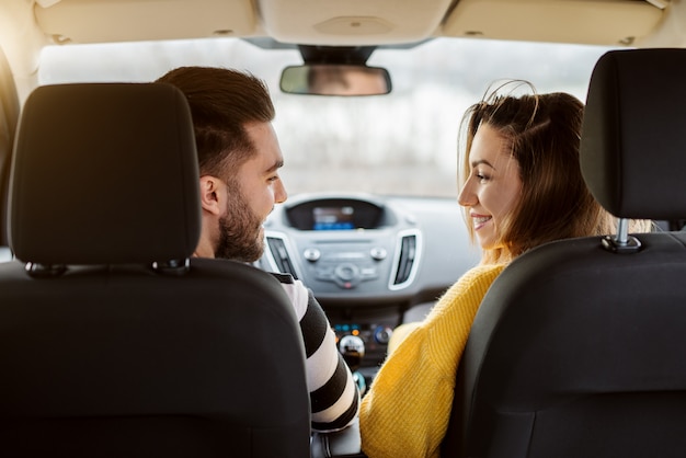 Vista posteriore in un'auto di belle giovani coppie felici di amore che si guardano.