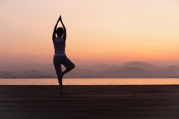 Vista posteriore integrale della donna in piedi su una gamba mentre si fa yoga all'alba