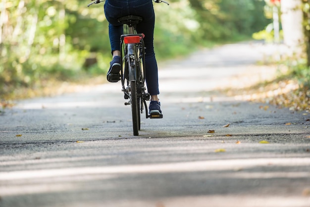 Vista posteriore ritagliata di una donna in sella a una bicicletta su un percorso all'aperto come allenamento cardio ricreativo