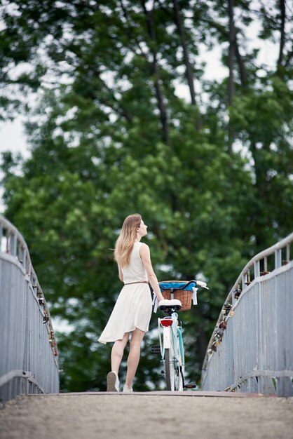 Vista posteriore snella femmina in piedi con la bicicletta e godersi la natura sul ponte