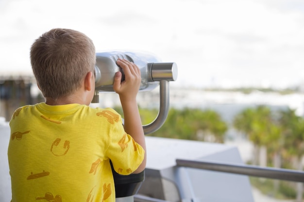 Vista posteriore sul ragazzo del bambino con il binocolo turistico che esamina la distanza. Esplorazione del bambino