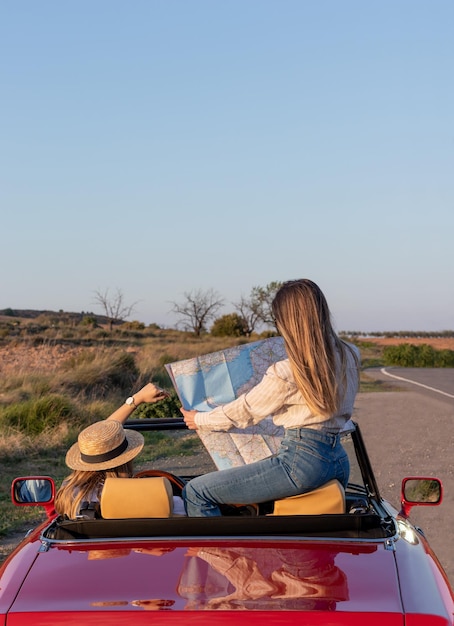 Vista posteriore verticale di amici irriconoscibili che leggono una mappa in un'auto convertibile retrò rossa