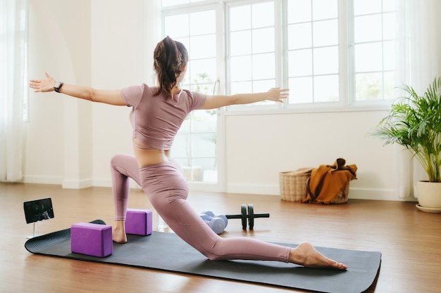 Vista rara bella donna asiatica che indossa abbigliamento sportivo che pratica yoga indoor a casa