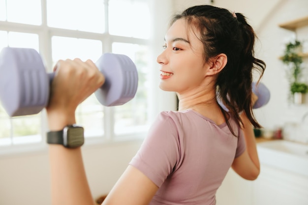 Vista rara di una bella donna asiatica che indossa un esercizio di abbigliamento sportivo con manubri al coperto a casa