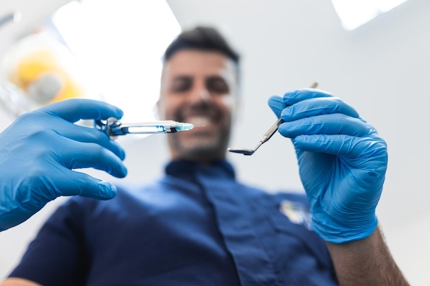 Vista ravvicinata dei pazienti di un dentista Bel dentista in guanti chirurgici tiene gli strumenti e guarda la fotocamera