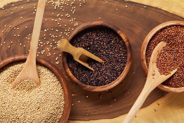 Vista ravvicinata dei semi di quinoa bianchi neri e rossi in ciotole di legno con spatola e cucchiai