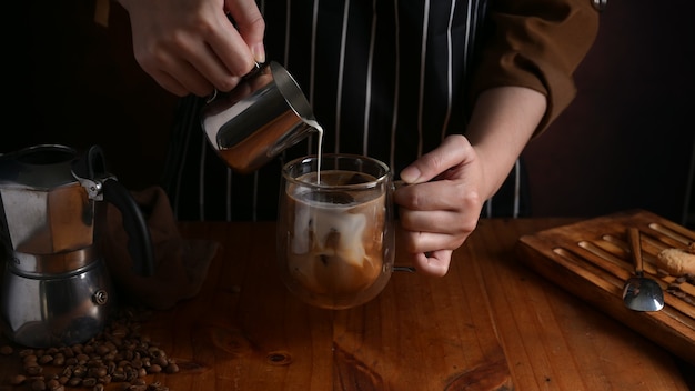 Vista ravvicinata del barista versando il latte in una tazza di caffè sul bancone in legno bar nella caffetteria