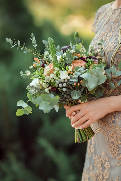 Vista ravvicinata del bellissimo bouquet da sposa colorato in una mano di una sposa contro il bokeh verde della natura dello sfondo