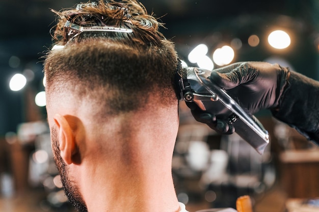 Vista ravvicinata del giovane uomo barbuto che si siede e si fa tagliare i capelli nel negozio di barbiere