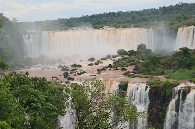 Vista ravvicinata del ponte di osservazione e dei ponti per i turisti dell'acqua Cataratas che cade sotto il cielo blu arcobaleno e una nebbia d'acqua al parco Foz do Iguassu