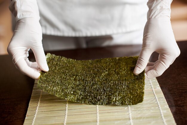 Vista ravvicinata del processo di preparazione del sushi di laminazione. Le mani dello chef tengono un foglio di nori e iniziano a cucinare