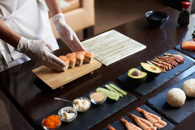 Vista ravvicinata del processo di preparazione del sushi di rotolamento. Lo chef serve deliziosi panini freschi sulla tavola di legno.