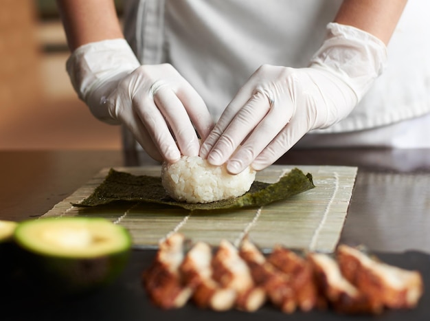 Vista ravvicinata del processo di preparazione del sushi di rotolamento. Nori e riso bianco su stuoia di bambù. Le mani dello chef toccano il riso. Lo chef inizia a cucinare il sushi. Anguilla e avocado