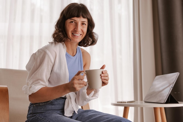 Vista ravvicinata della donna caucasica che sorride alla telecamera tenendo una tazza di caffè