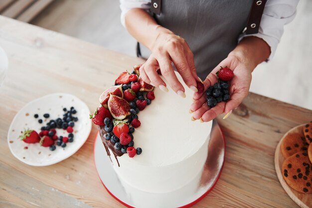 Vista ravvicinata della donna che mette le ciliegie sulla torta dolce.