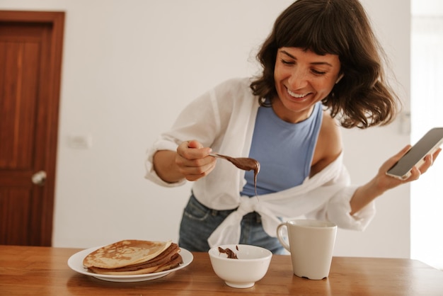 Vista ravvicinata della donna sorridente che mangia in cucina e orza con il telefono