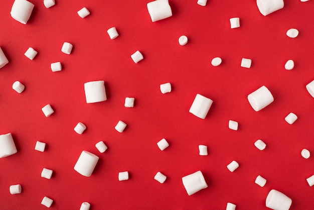 Vista ravvicinata della foto di un gustoso marshmallow di dimensioni diverse piccole e grandi che giace su uno sfondo rosso di colore vivido