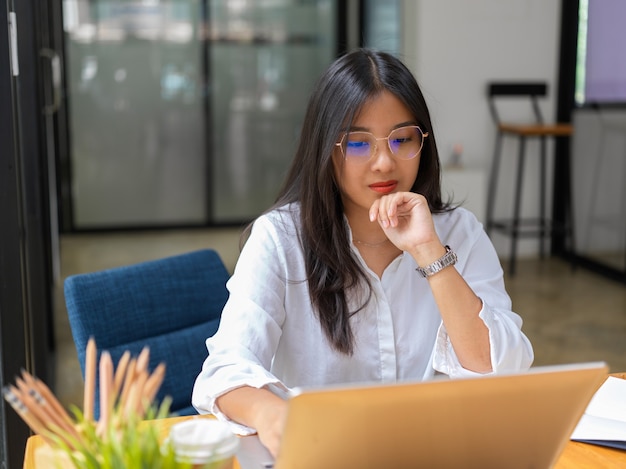 Vista ravvicinata della lavoratrice concentrandosi sul suo lavoro con laptop e forniture in ufficio