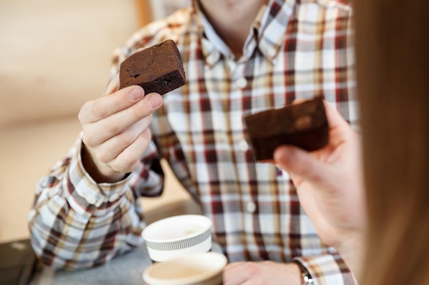 Vista ravvicinata della mano dell'uomo che tiene la torta brownie mentre beve caffè