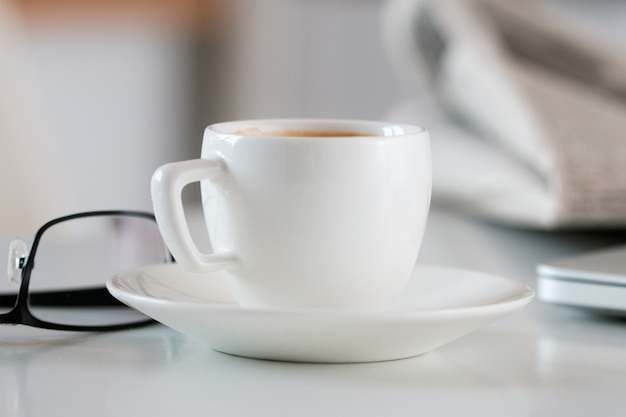 Vista ravvicinata della tazza di caffè bianco sul tavolo con gli occhiali