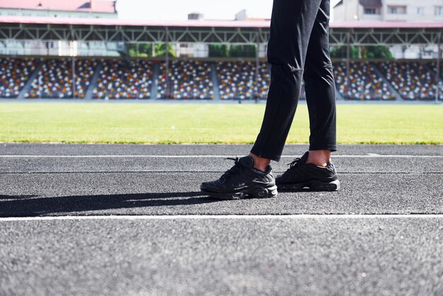 Vista ravvicinata delle gambe del corridore in pantaloni neri e scarpe che è all'aperto in pista