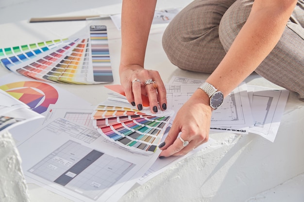 Vista ravvicinata delle mani della donna designer di interni che lavorano con la tavolozza dei colori e piani interni per un nuovo progetto con soft focus.