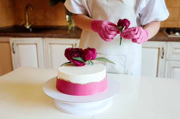 Vista ravvicinata delle mani della donna in guanti decorare bella torta con peonie
