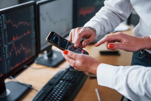 Vista ravvicinata delle mani delle persone con telefono e grafici su di esso. Gli agenti di cambio hanno un lavoro.